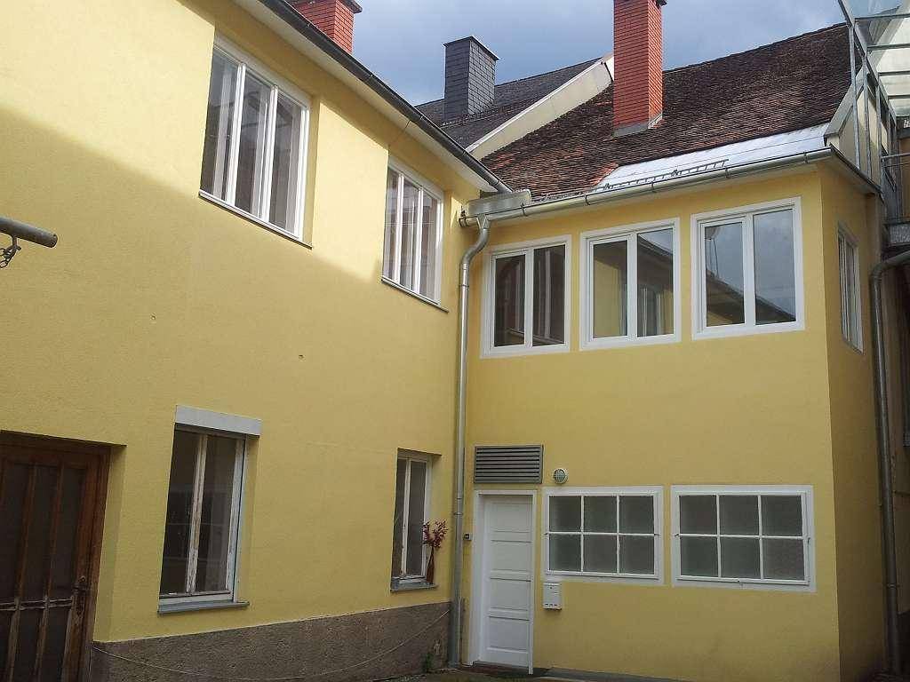 Gelb gestrichene Gebäudefassade mit mehreren Fenstern und einem Eingangsbereich im Hinterhof.