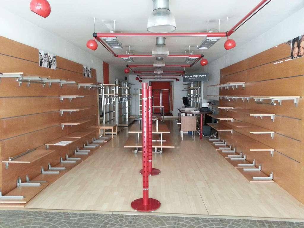 Leerer Ladenraum mit Holzregalen an den Wänden und einer modernen Beleuchtungsanlage.