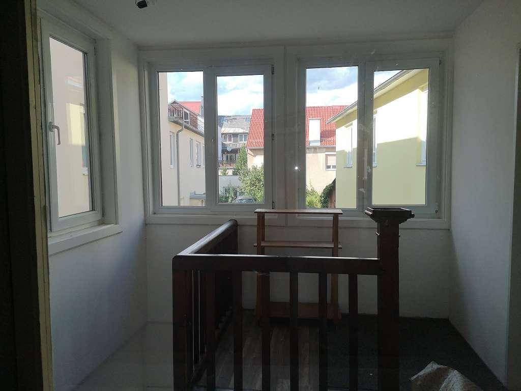 Heller Flurbereich mit großen Fenstern und einem Holzgeländer, das einen Blick nach draußen bietet.
