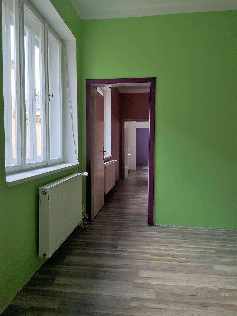 Innenraum mit leuchtend grünen Wänden, einem Holzboden und einem Heizkörper unter dem Fenster.