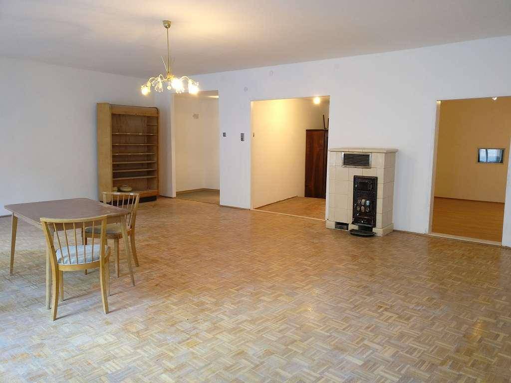 Geräumiges Wohnzimmer mit Parkettboden, einem Esstisch und einem traditionellen Kachelofen.