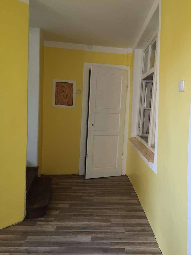 Heller Flur mit gelben Wänden, einem Holzboden und einem Fenster, das Tageslicht hereinlässt.