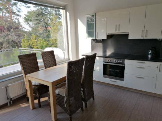 Moderne Küche mit weißen Schränken, Essbereich und großem Fenster mit Blick ins Grüne.