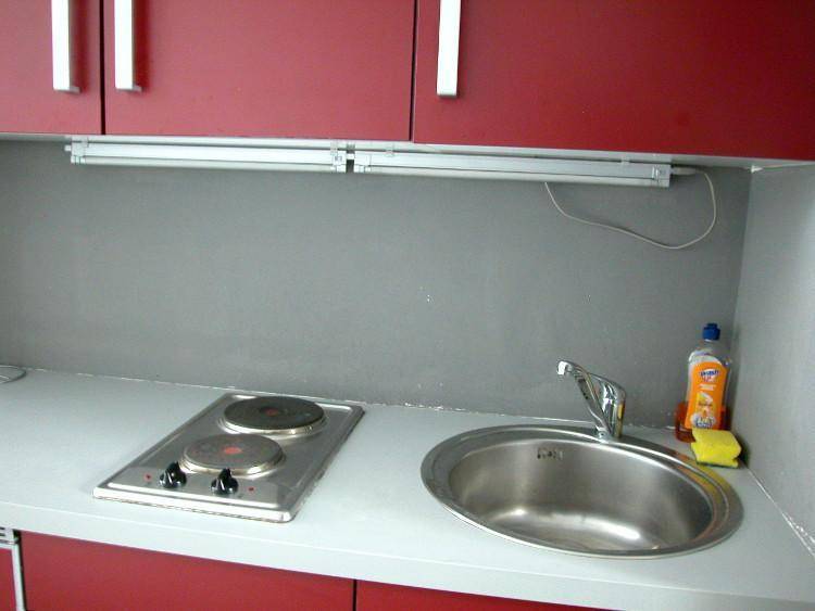 Nahaufnahme der Küchenzeile mit Spülbecken, zwei elektrischen Kochplatten und roten Oberschränken.