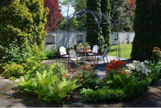 Gepflegter Gartenbereich mit einem Pavillon, Sitzgelegenheiten und üppiger Bepflanzung.