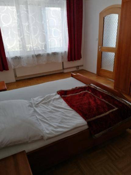 Detailansicht eines Bettes in einem Schlafzimmer mit Fenster und roten Vorhängen.