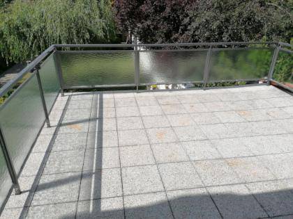 Geräumige geflieste Terrasse mit moderner Glasbrüstung und Blick ins Grüne.