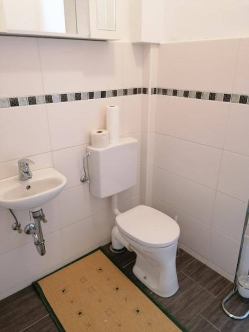 Kleines Gäste-WC mit Toilette, Waschbecken und Wandfliesen.