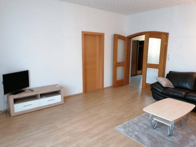 Heller Wohnbereich mit TV-Möbeln, Sofa und Holztüren, die zu weiteren Räumen führen.