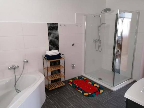 Duschkabine und Eckbadewanne in einem hell gefliesten Badezimmer mit farbigem Teppich.