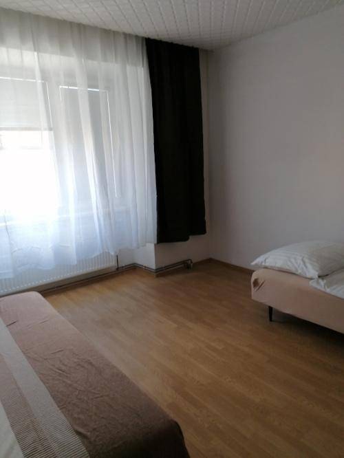 Helles Schlafzimmer mit einem Bett, großem Fenster und hellem Laminatboden.