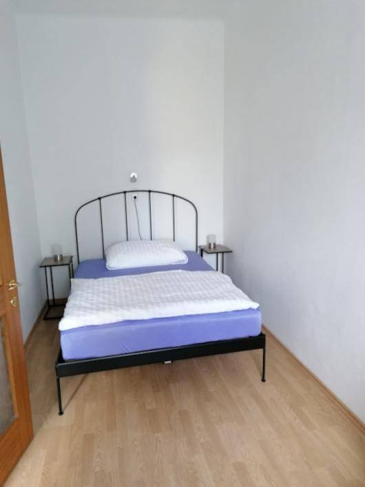 Schlafzimmer mit modernem Metallbettgestell, kleinen Nachttischen und hellem Laminatboden.