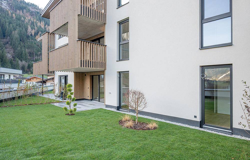 Kleiner privater Gartenbereich mit Terrasse und jungem Baum, direkt am modernen Wohngebäude gelegen.