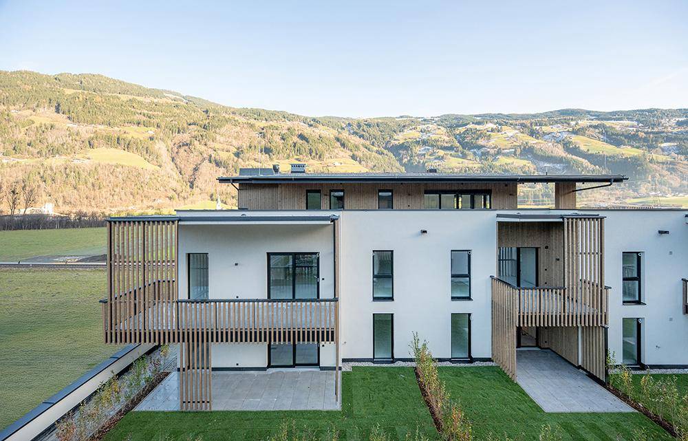 Moderne Wohngebäude mit großzügigen Balkonen und Terrassen, umgeben von Rasenflächen und Bergen.