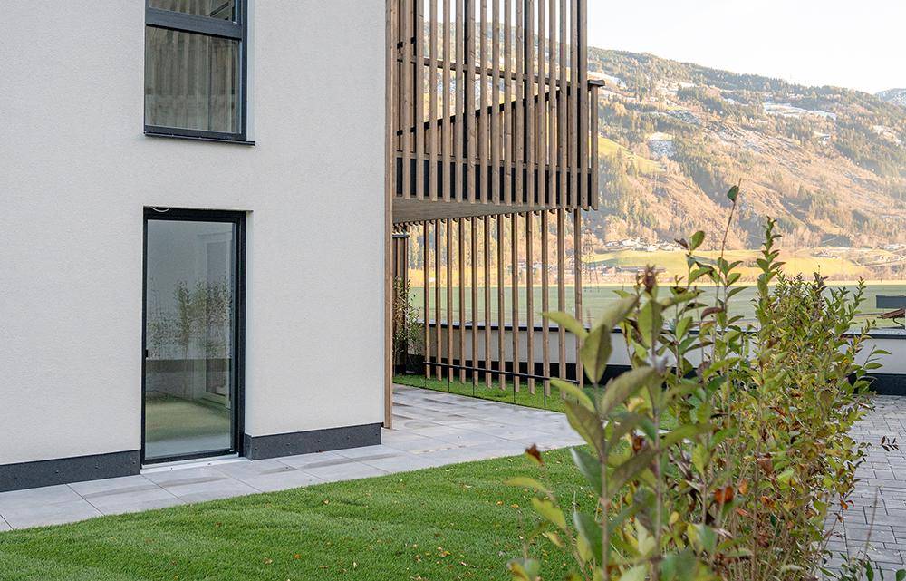 Detailansicht der modernen Fassade mit großen Fenstern und Blick auf die grüne Berglandschaft.