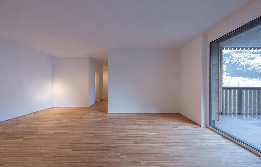 Helles Wohnzimmer mit Holzboden und großem Fenster, das Zugang zu einem Balkon bietet.