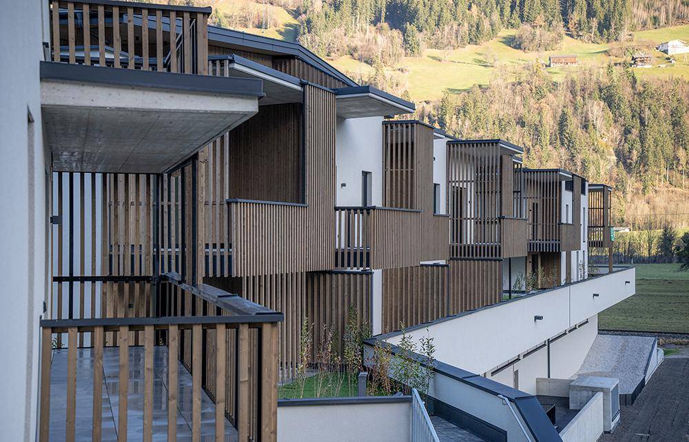 Seitenansicht der modernen Wohnanlage mit gestaffelten Balkonen und Blick auf die bewaldeten Hügel.