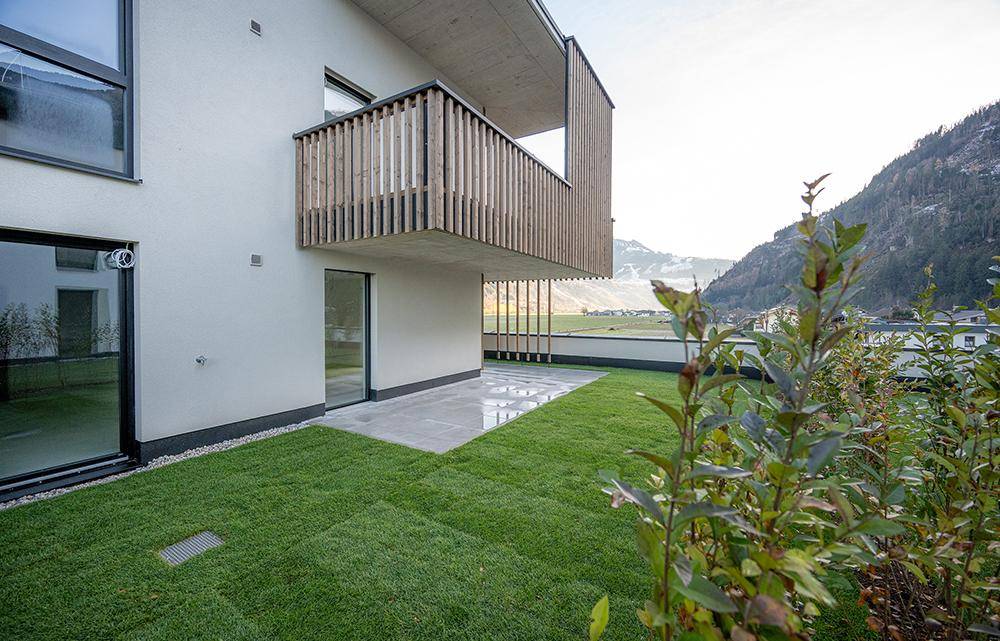 Private Gartenfläche mit Rasen und einer gepflasterten Terrasse, ergänzt durch einen Balkon im Obergeschoss.