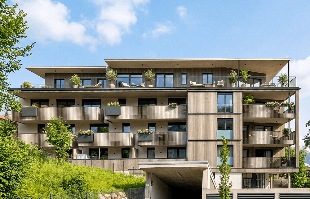 Moderne Wohnanlage mit Holzfassade, großen Balkonen und Tiefgaragenzufahrt in grüner Umgebung.
