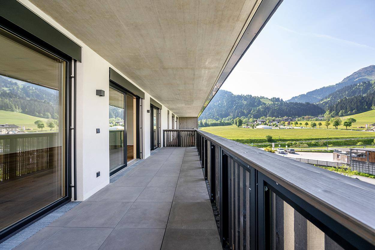 Langer Balkon mit Fliesenboden und weitem Blick auf die umliegende grüne Landschaft und Berge.