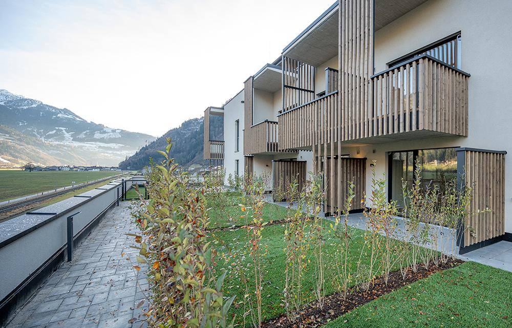 Ansicht der modernen Wohngebäude mit Holzlamellen, privaten Terrassen und Balkonen, eingebettet in eine grüne Umgebung.