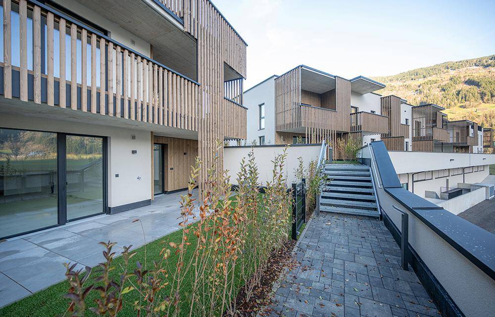 Moderne Fassade mit Holzlamellen, Außentreppe und Zugang zu den Erdgeschossgärten mit Bergblick.