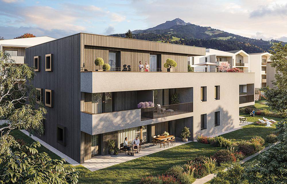 Moderne Wohnanlage mit Balkonen und Terrassen, eingebettet in eine grüne Landschaft mit Bergblick.