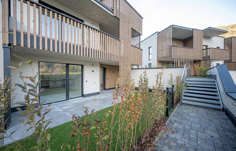Moderne Wohnanlage mit Holzfassadenelementen, begrüntem Gartenbereich und Außentreppe.