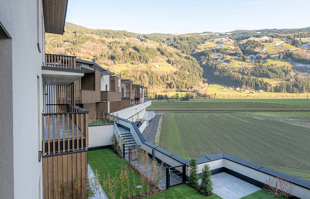 Weitläufige Ansicht einer modernen Wohnanlage mit Terrassen und Balkonen vor einer weiten Berglandschaft.