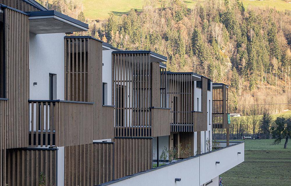 Detailansicht der modernen Balkone mit vertikalen Holzlamellen und Blick auf bewaldete Hügel.