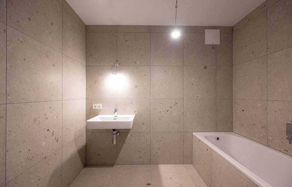 Modernes Badezimmer mit großformatigen Fliesen, Waschbecken und Badewanne.