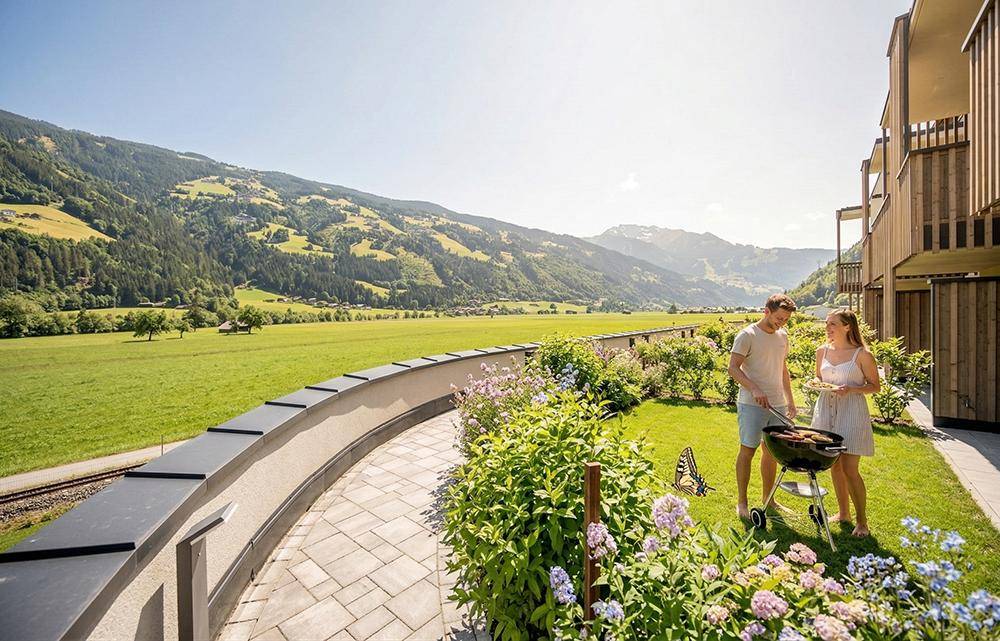 Sonniger Gartenbereich mit Grillplatz und weitem Blick auf die umliegende Berglandschaft.