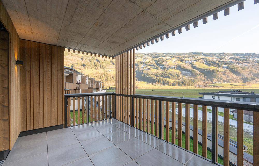Geräumiger Balkon mit Fliesenboden und Holzelementen, bietet weiten Blick auf die Berge.