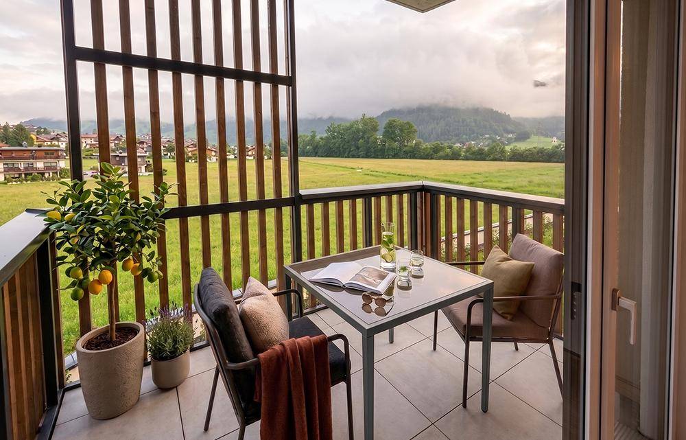 Gemütlicher Balkon mit Sitzgelegenheiten und weitem Blick über grüne Felder und Berge.