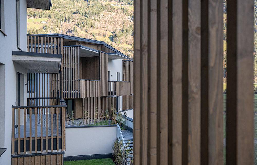 Detailansicht der modernen Holzlamellenfassade und der Balkone mit Blick auf die umliegenden Berge.