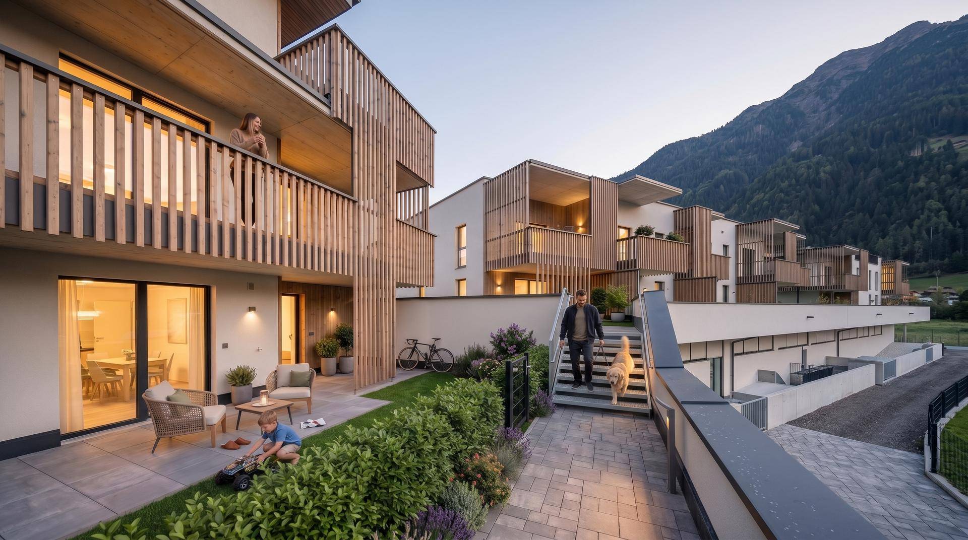 Moderne Wohnanlage mit Terrassen und Balkonen, umgeben von grüner Landschaft und Bergen.