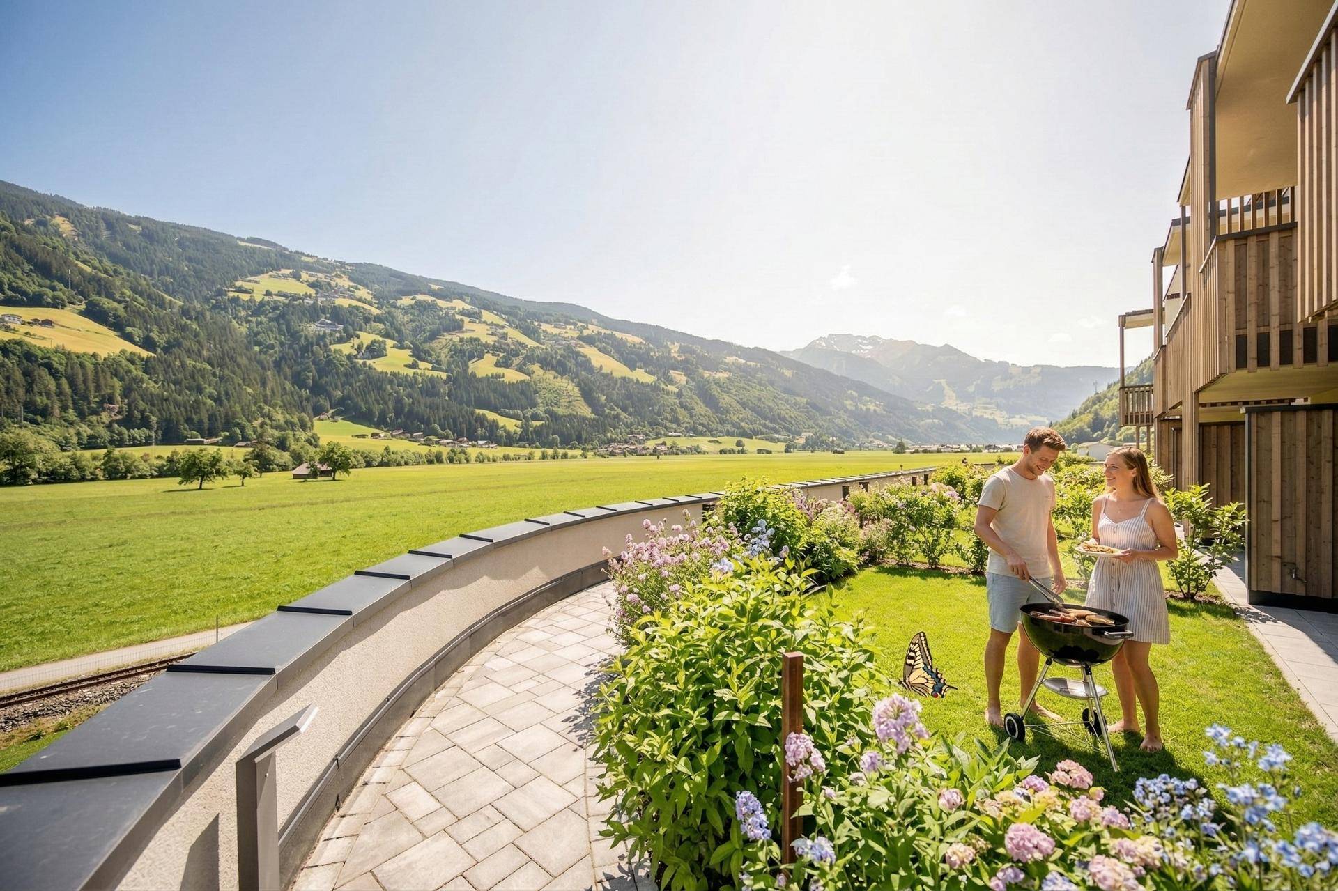 Sonnige Gartenfläche mit Grillbereich und weitem Blick auf die grüne Berglandschaft.