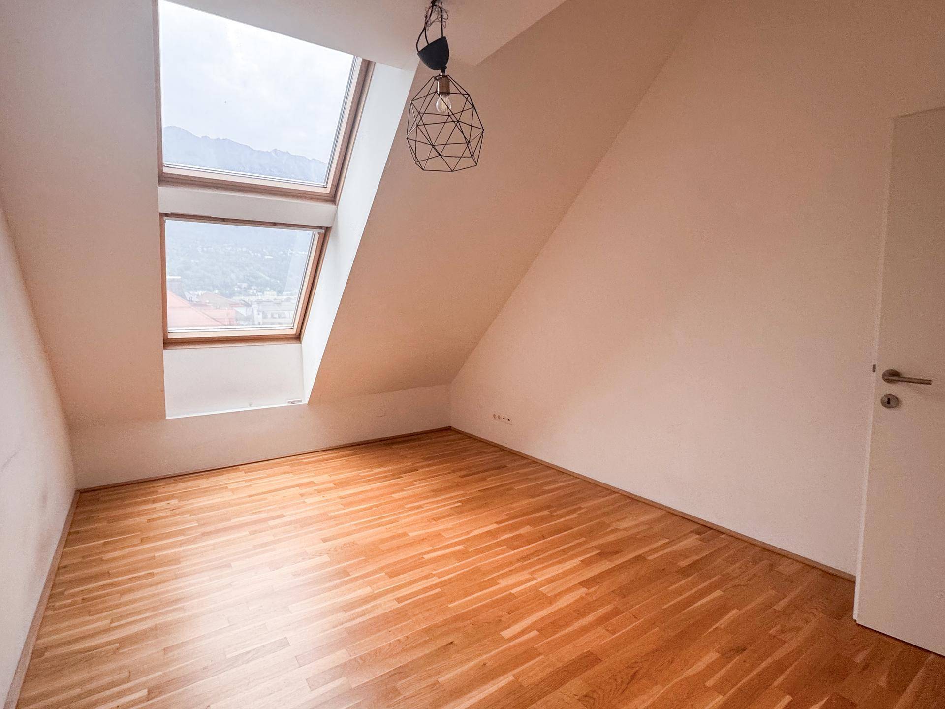 Helles Dachzimmer mit Holzboden, weißen Wänden und zwei großen Dachfenstern für viel Tageslicht.