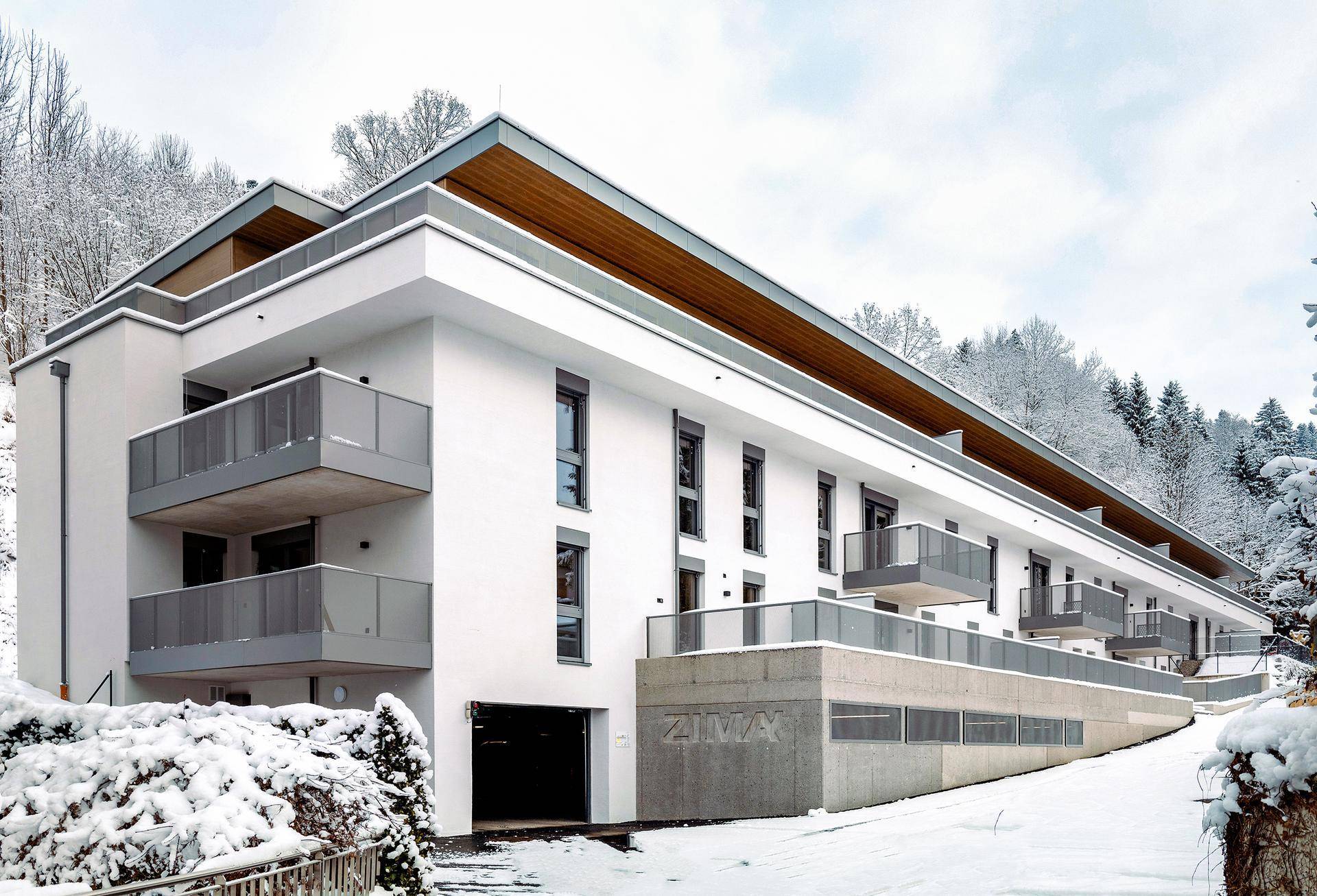 Elegantes Mehrfamilienhaus in moderner Architektur, umgeben von winterlicher Schneelandschaft und Bäumen.