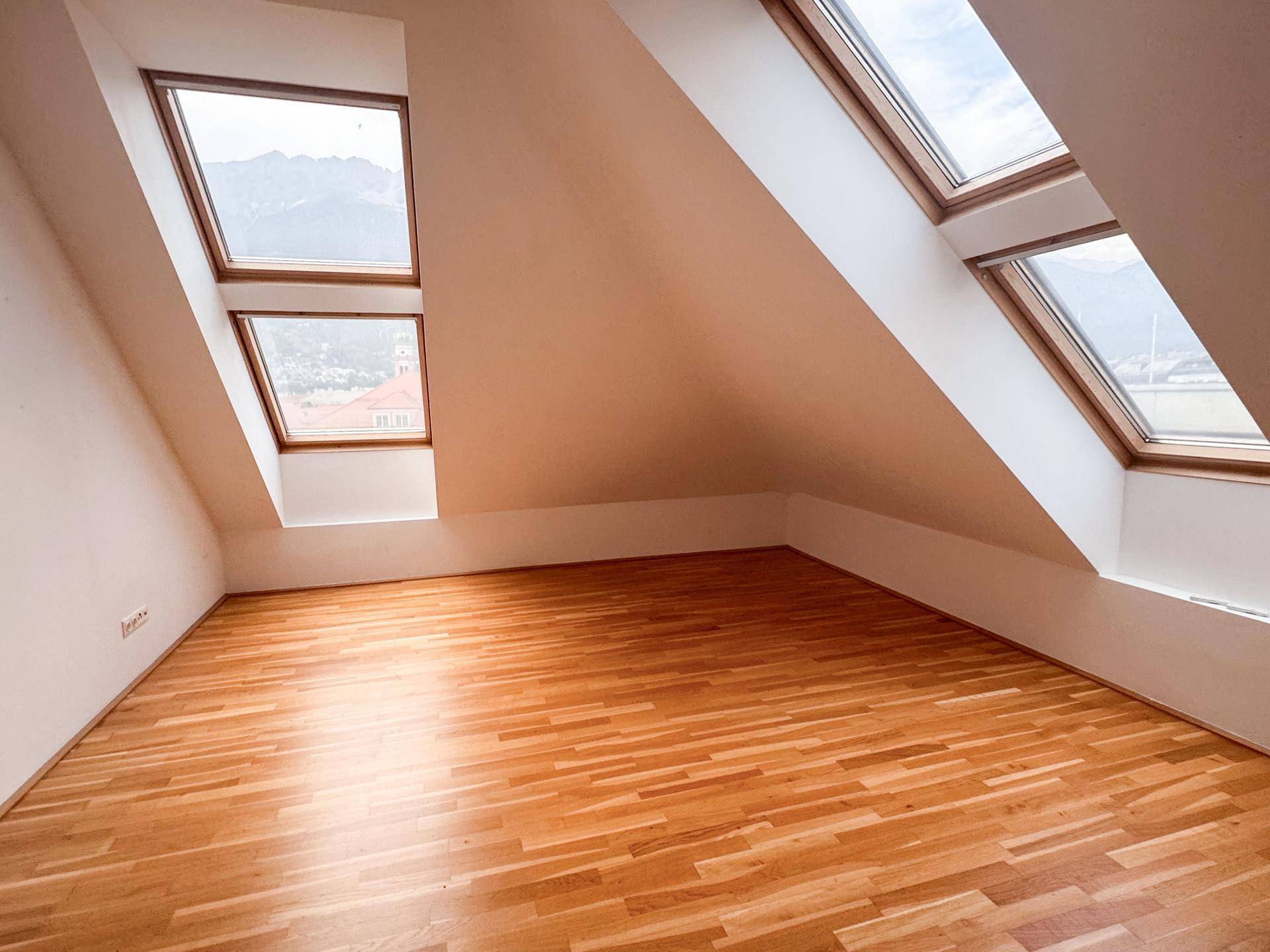 Lichtdurchflutetes Zimmer im Dachgeschoss mit Parkettboden und mehreren Dachfenstern mit Bergblick.