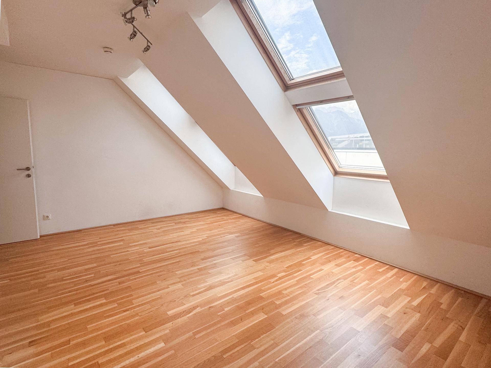 Geräumiges Dachzimmer mit hellem Holzboden und drei Dachfenstern, die einen weiten Blick bieten.
