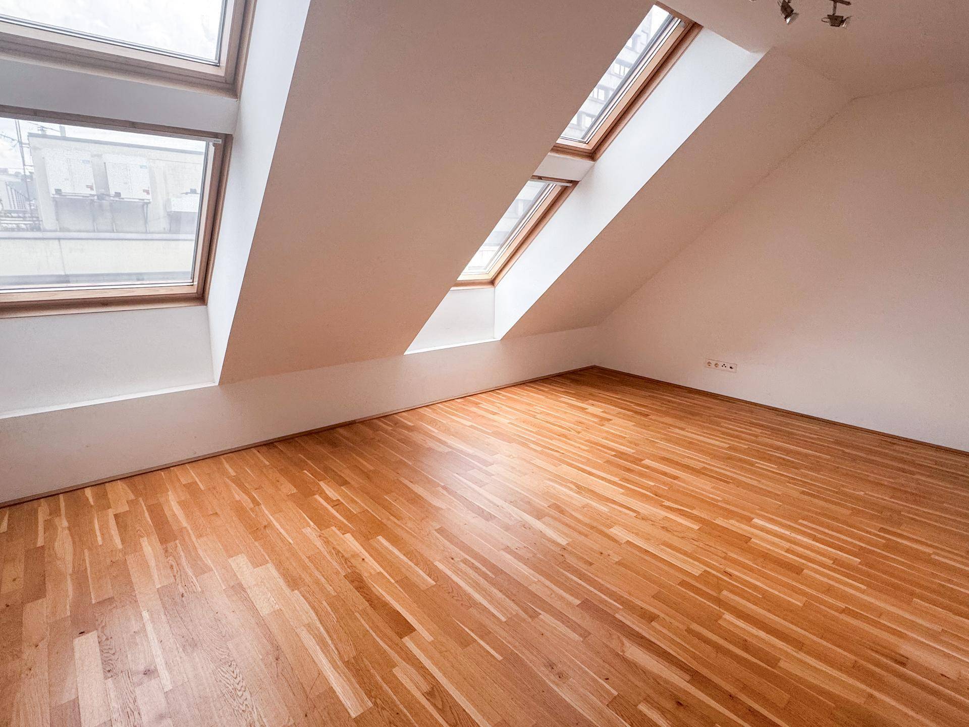 Geräumiges Zimmer im Dachgeschoss mit Parkettboden und mehreren Dachfenstern, die den Raum erhellen.