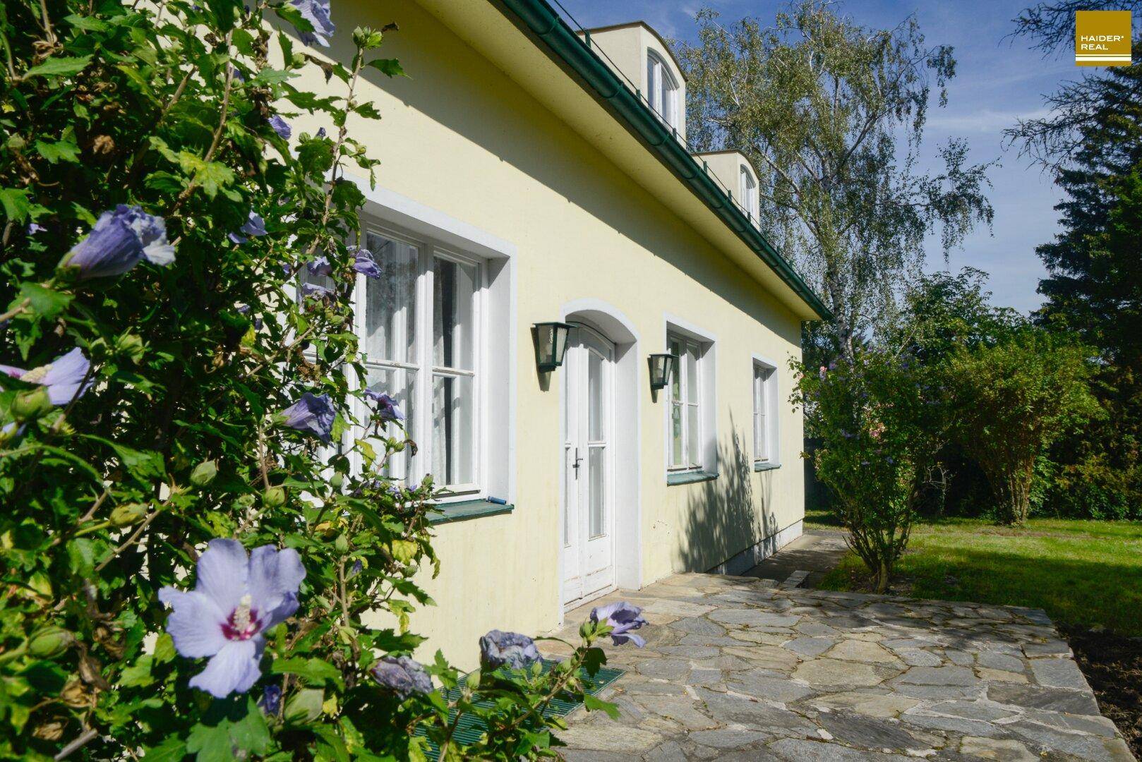 Detailansicht der Hausfassade mit Eingangstür, Fenstern und blühenden Pflanzen im Vordergrund.