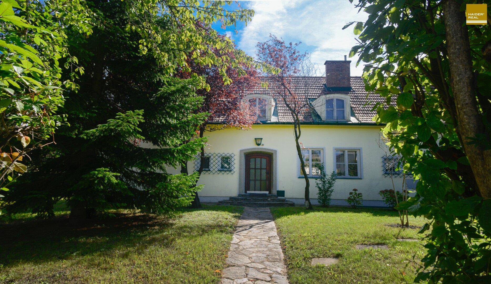 Vorderansicht des Hauses mit gepflastertem Weg, umgeben von Bäumen und einem gepflegten Rasen.