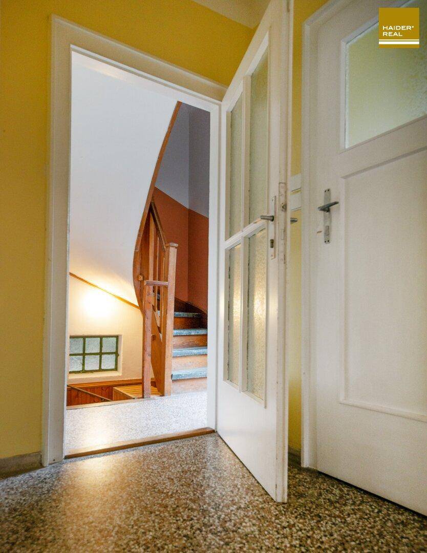 Heller Flur mit Terrazzoboden und einer Holztreppe, die in die oberen Stockwerke führt.