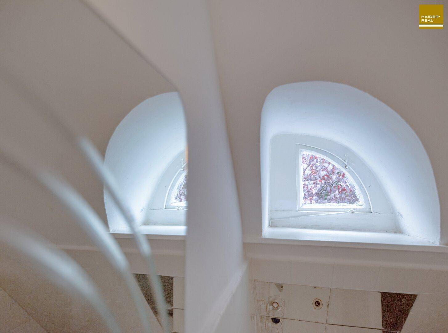 Zwei kleine, gewölbte Fenster mit Blick ins Grüne, die natürliches Licht hereinlassen.