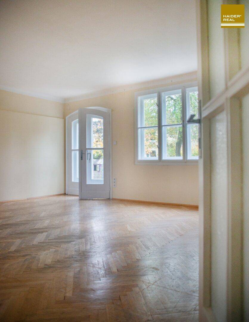 Helles, leeres Zimmer mit Fischgrätparkettboden und Doppeltür zum Gartenbereich.