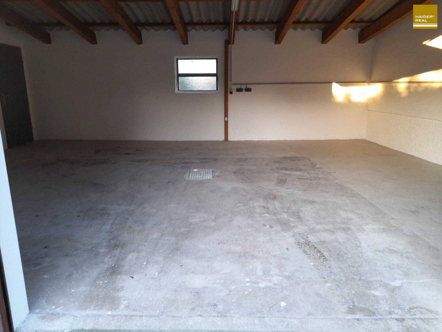 Saubere Garage mit Betonboden, Holzbalkendecke und einem kleinen Fenster für Tageslicht.