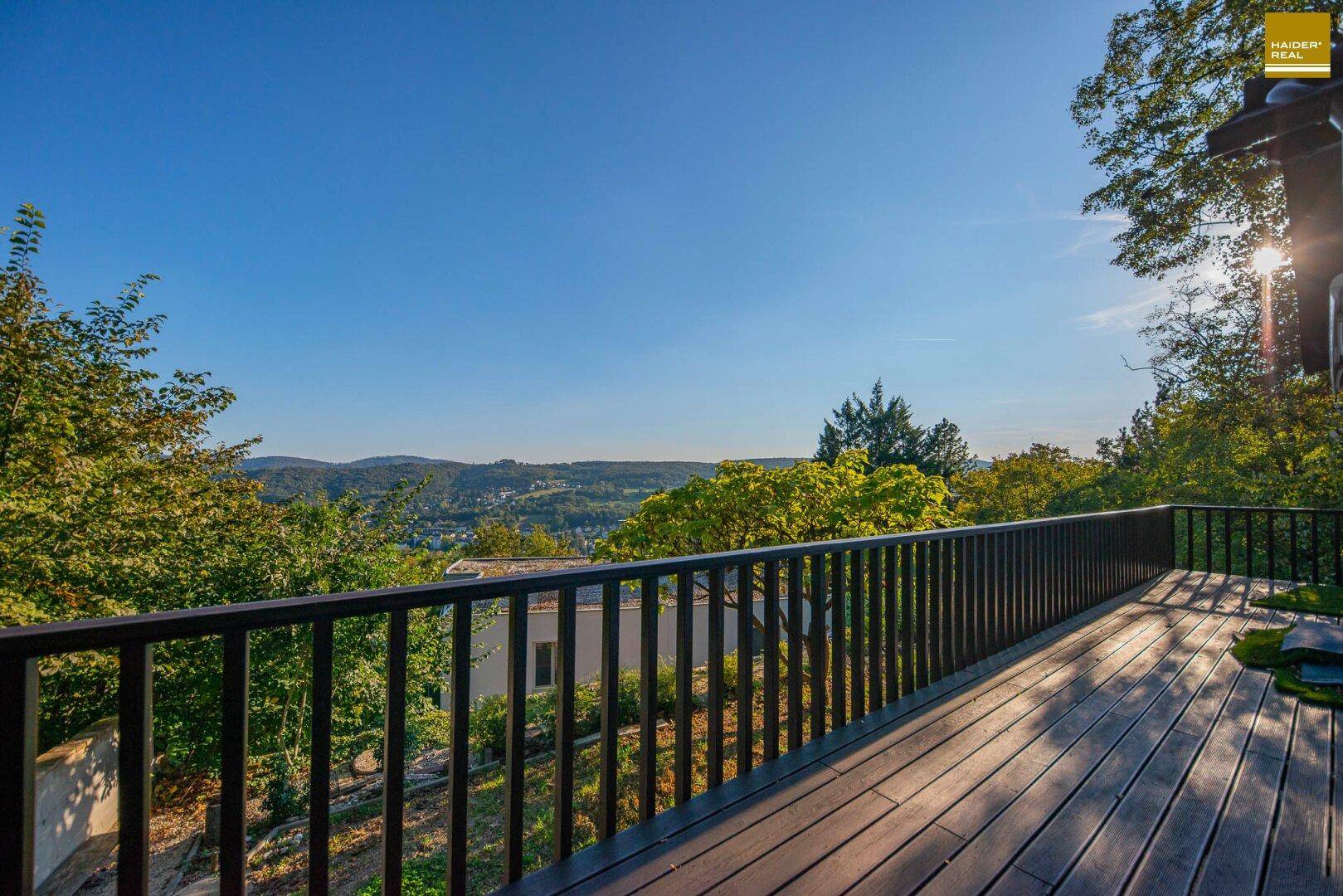 Geräumige Holzterrasse mit schwarzem Geländer und weitem Blick über die Landschaft.