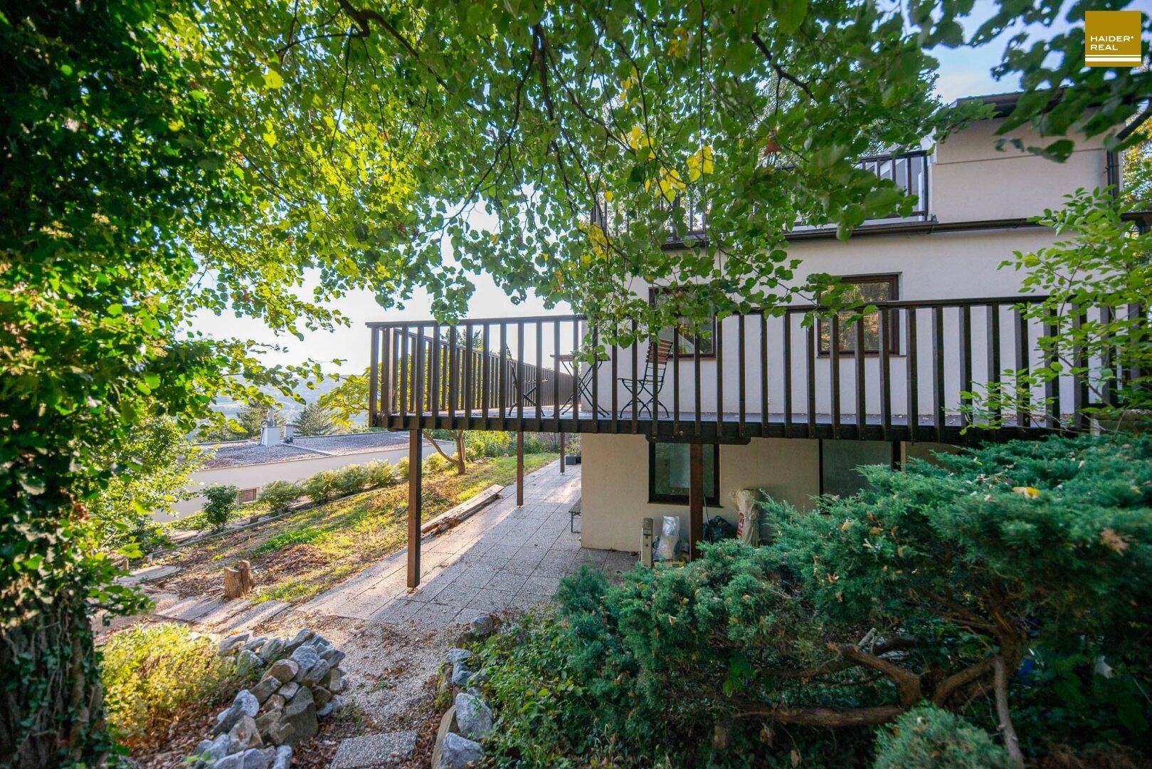 Balkon mit Holzgeländer und darunterliegender Terrasse, umgeben von üppigem Grün.
